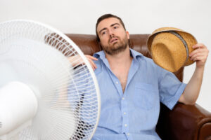 Why Is My Air Conditioner Blowing Hot Air? Flushed man feeling hot in front of a fan.