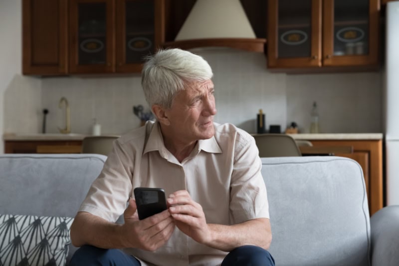 What’s That Smell Coming From My Furnace? Photo of a man on his phone sitting on his couch, looking out the window seemingly concerned.