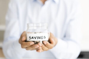 Why Buying a Heat Pump Instead of a Furnace Makes Sense. Photo of a person holding a jar of coins labeled "Savings".